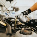 Close-up of a mechanic pouring engine oil into a car engine in an auto repair shop.